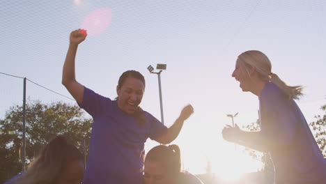 excited womens soccer team celebrating winning game picking up player and carrying on shoulders