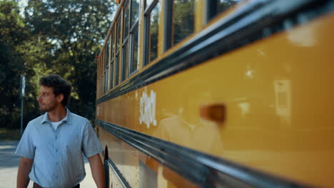 Young-schoolbus-driver-walking-along-yellow-vehicle.-Focused-man-posing-near-car