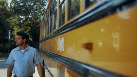 young schoolbus driver walking along yellow vehicle. focused man posing near car