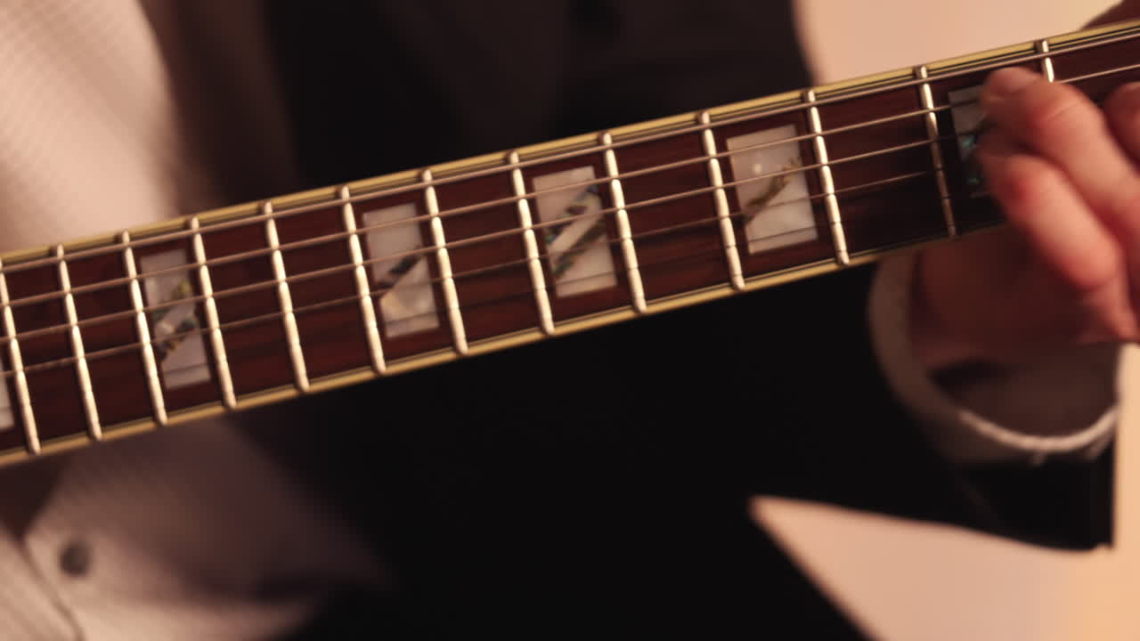 Primissimo piano della mano di un chitarrista jazz sulla tastiera mentre la telecamera si sposta leggermente verso l'alto per seguire il movimento