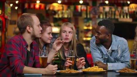 una gran compañía alegre de jóvenes en el bar charlando discutiendo el semestre los últimos rumores riendo y bebiendo cerveza. compañía multiétnica.