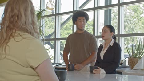 three workers in their 20's talking in an office setting with stable over the shoulder shot