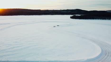 toma de drones de dos autos deportivos conduciendo en un lago congelado durante la puesta de sol