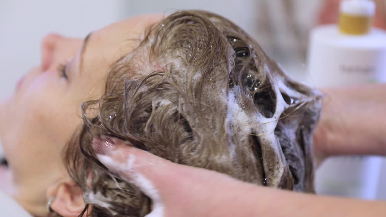 Concetto di bellezza, cura dei capelli e persone - giovane donna felice che si lava i capelli con lo shampoo dal parrucchiere
