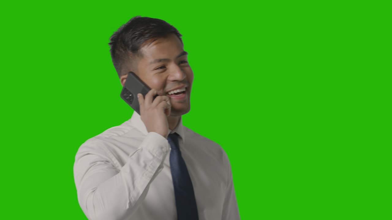 ripresa in studio di uomo d'affari sorridente in giacca e cravatta che parla al cellulare contro lo schermo verde 1