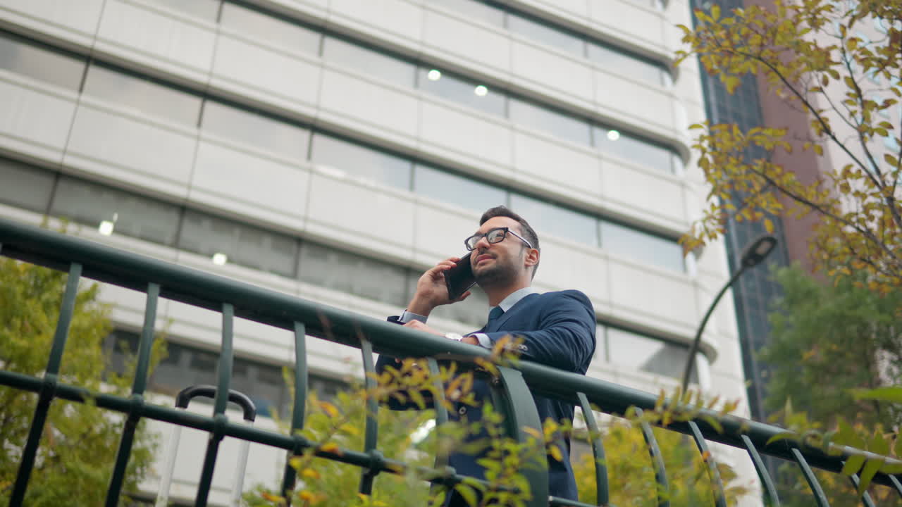 hombre de negocios apoyado contra la barandilla, hablando por teléfono