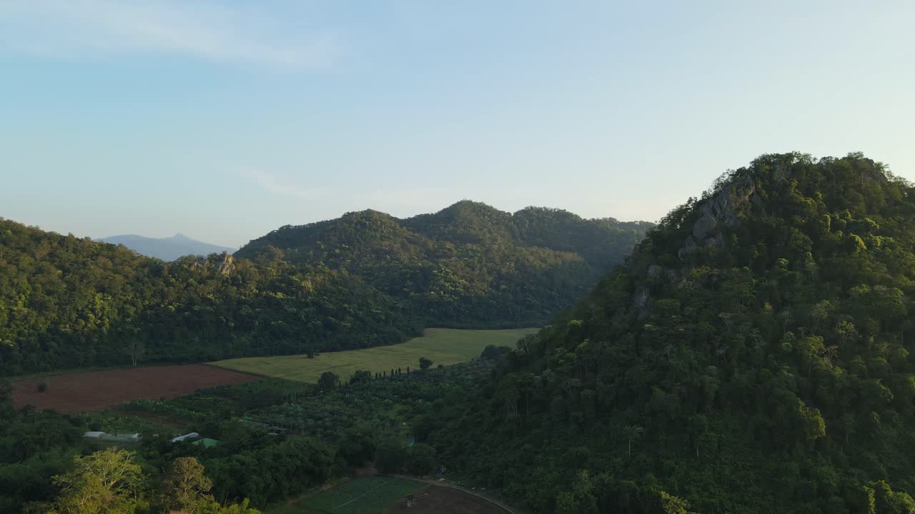 Aerial footage towards a valley with farms and the hills surrounding it with lovely blue sky in Pakchong, Khao Yai, Thailand