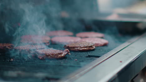 a mouthwatering view of delicious hamburgers sizzling on a bbq grill, surrounded by thick smoke and flames licking the burgers. the camera slowly moves in.