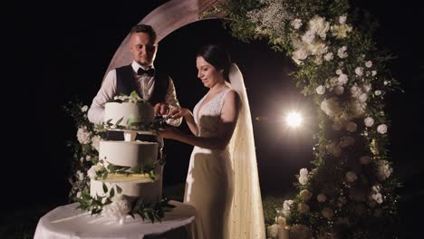 newlyweds cut the wedding cake, lovely bride and groom couple cutting dessert with a knife outdoors