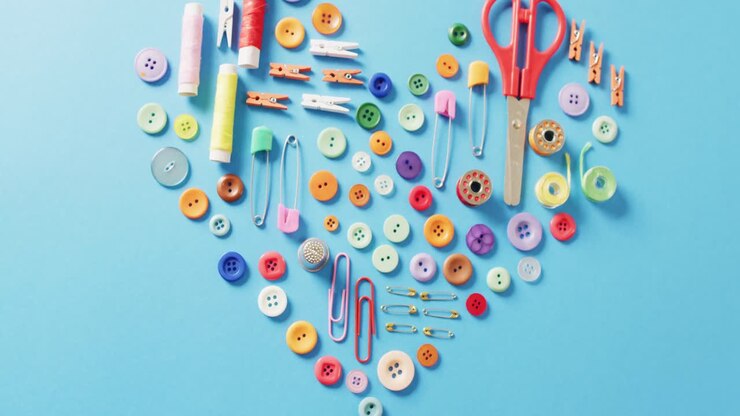Video of scissors, buttons, pins, clips, pegs and cotton reels in a heart shape on blue background