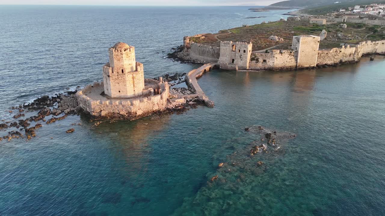 Methoni,Messenia,Peloponnese,Aerial view birds eye view circular pan left around Bourtzi Tower surrounded by crystal clear waters than forward towards the Methoni Castle and over during golden hour