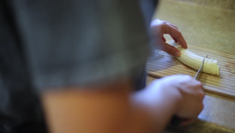 Over-the-Shoulder-Slow-motion-shot-of-someone-using-a-knife-to-cut-a-ripe-yellow-banana-into-small-slices