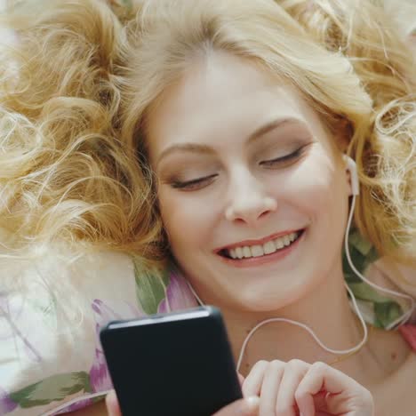 a woman with beautiful hair lies on a pillow uses a smartphone