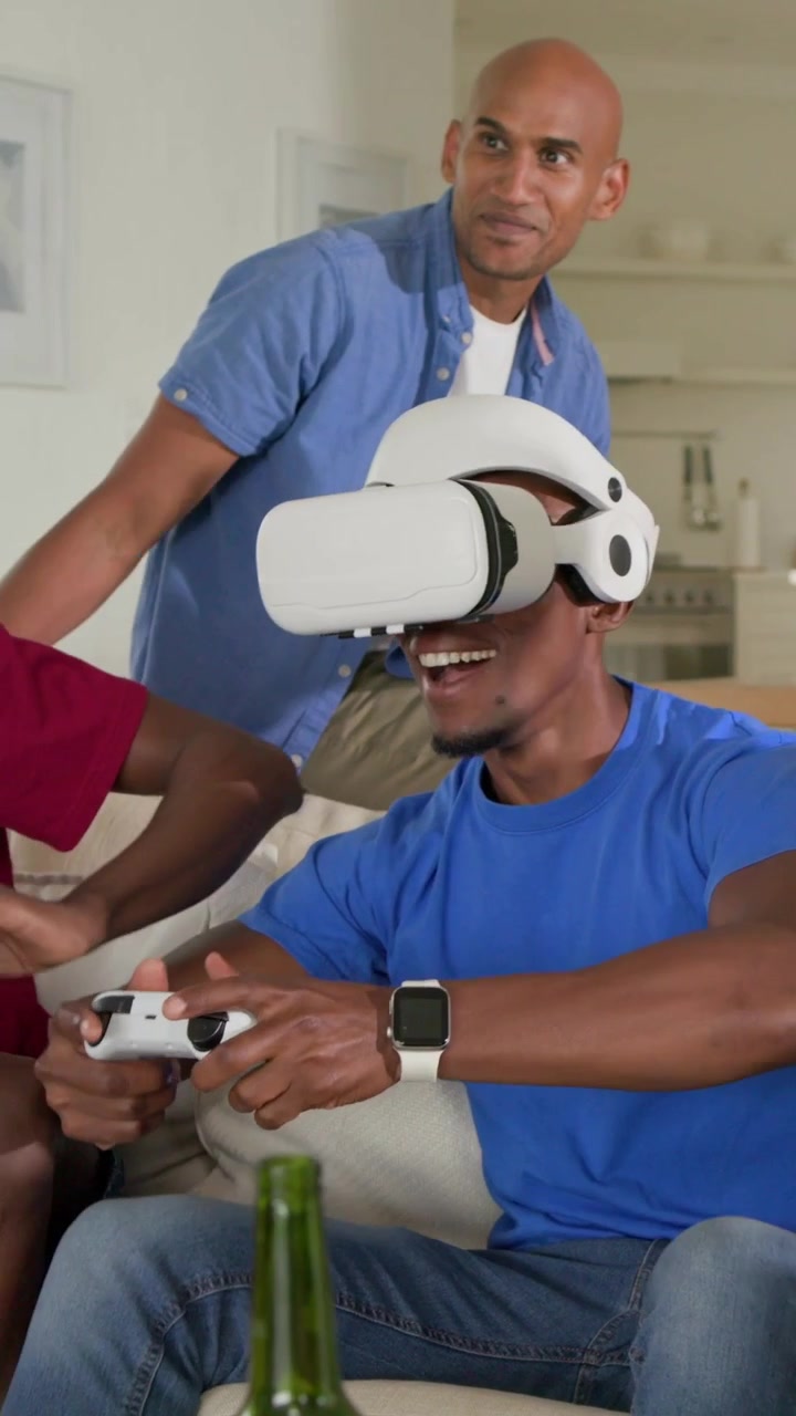 Video verticale: Uomo che indossa un visore VR bianco e manipola un controller a casa per il gioco di gruppo.