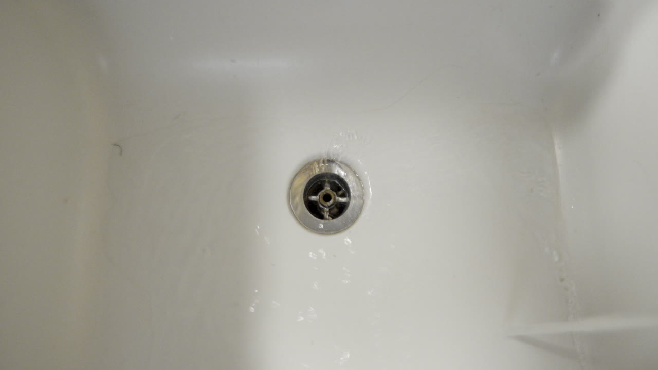 A person tries to clear a clogged bathtub drain using a waste bell
