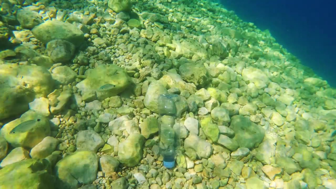 Una bottiglia di plastica giace sul fondale oceanico tra rocce e ghiaia. I detriti marini impattano la vita acquatica e gli habitat. La consapevolezza dell'inquinamento da plastica è essenziale per gli sforzi di conservazione
