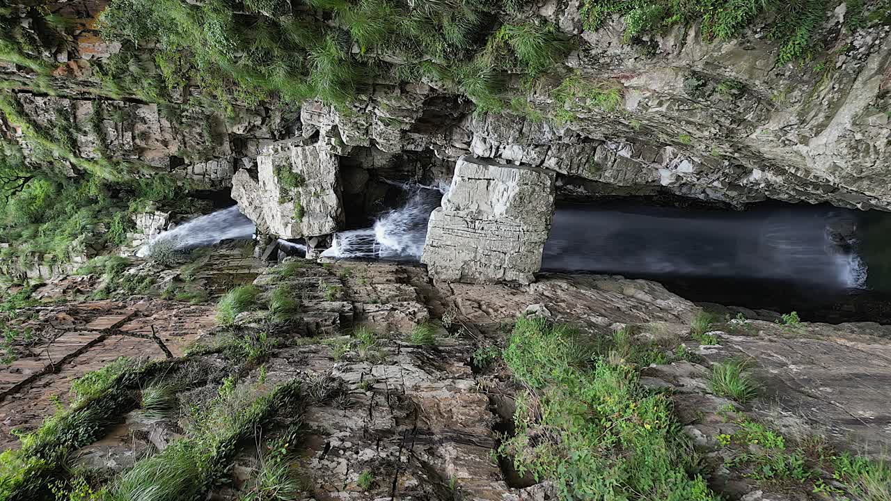 Gros blocs de pierre coincés dans une gorge rocheuse étroite avec une cascade, vue aérienne.