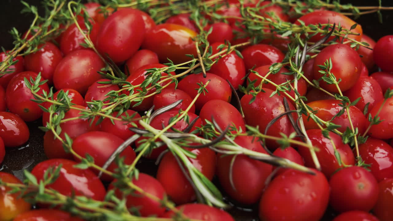 Bright red cherry tomatoes in a cast-iron pan, covered with rosemary and thyme