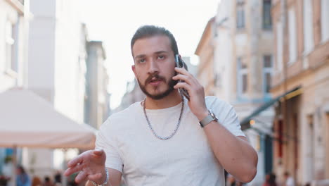 happy young man having remote conversation talking on smartphone good news gossip in city street