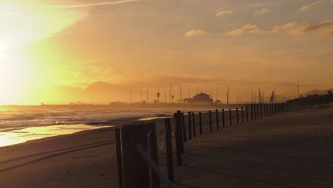 Blick-Auf-Den-Strand-Bei-Sonnenaufgang-An-Der-Küste-Mit-Zaunpfosten,-Die-Sich-In-Die-Ferne-Erstrecken