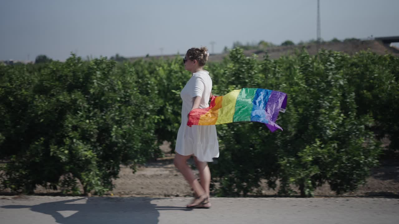 Woman walking with pride flag in an orchard