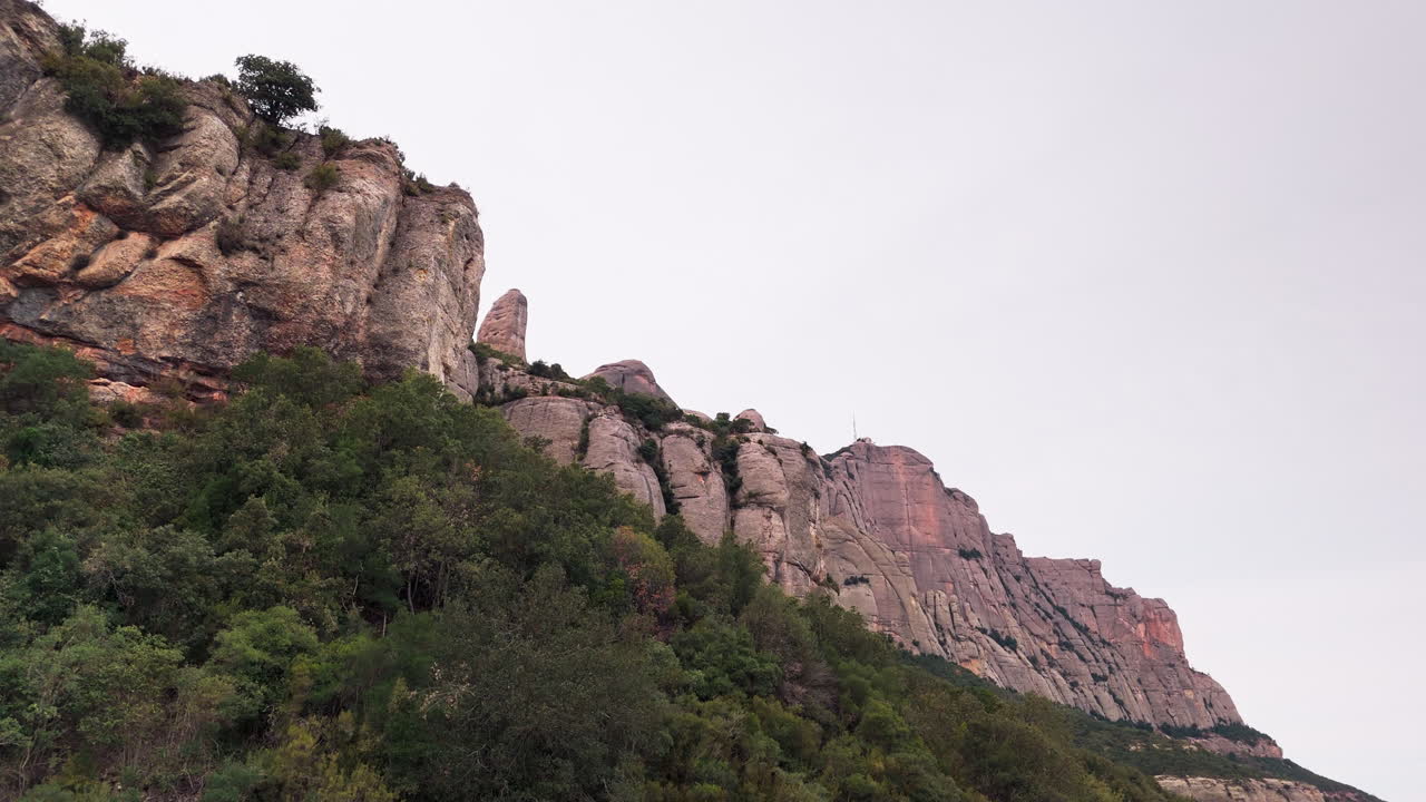 una toma de una grúa drone que revela con gracia los picos redondos de los acantilados de montserrat en el telón de fondo de un tranquilo día nublado