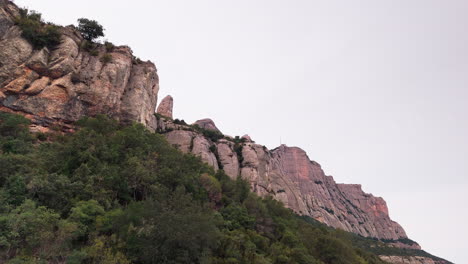 Drone-crane-up-shot-gracefully-revealing-the-round-cliff-peaks-of-Montserrat-against-the-backdrop-of-a-tranquil-overcast-day