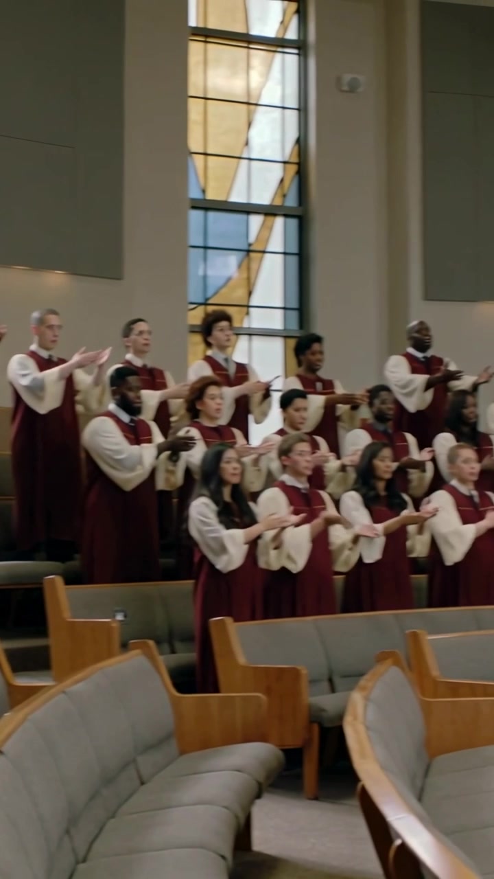 Vertical video: Camera pulling back causing choir in burgundy robes gesturing on risers in worship