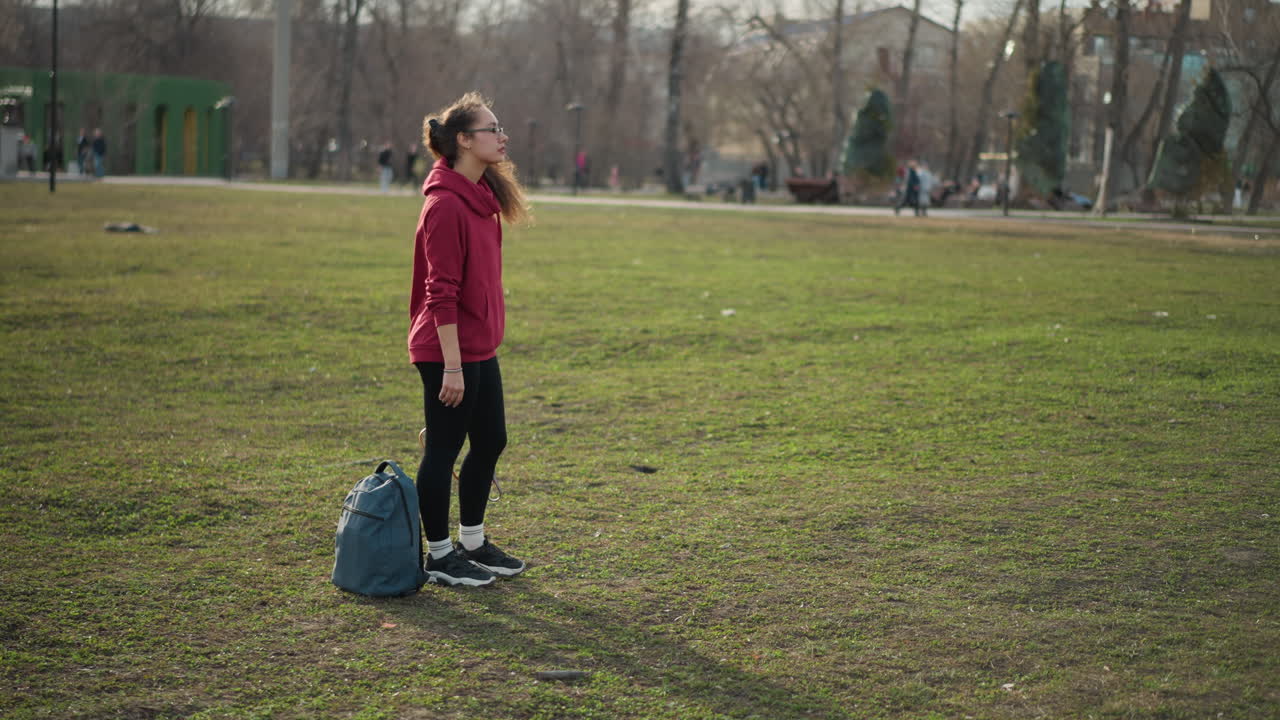 Individual Reflects In Sunlit Outdoor Space, Youth Standing Thoughtfully With Backpack In Peaceful Park Setting, Student Wearing Hoodie Contemplates Near Play Area Under Gentle Sunlight