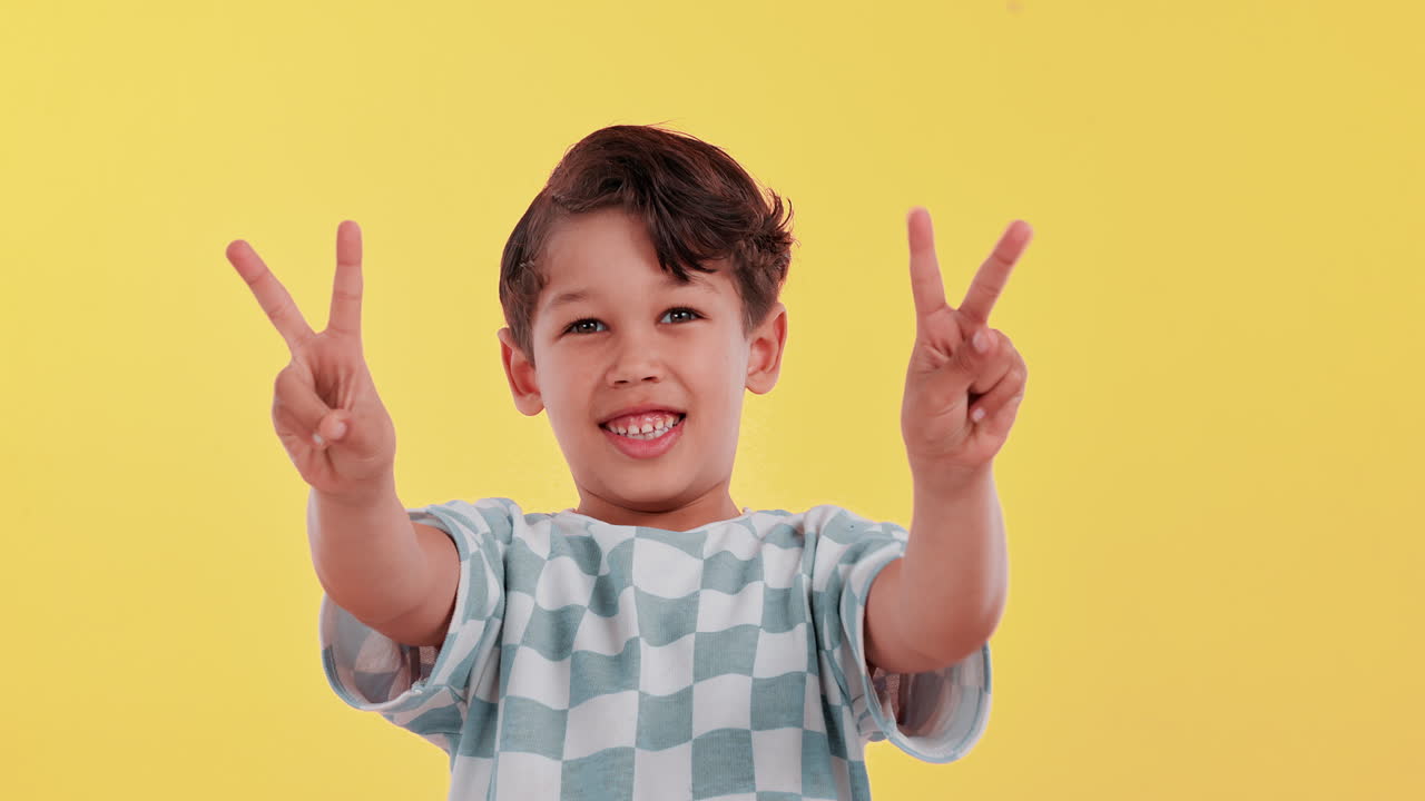 A smiling child making a peace sign in front of a yellow background