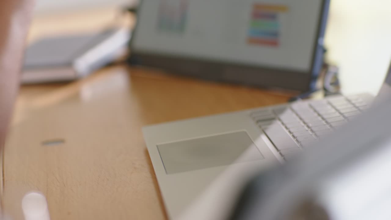 Mano destra che digita e tocca laptop e monitor mentre risponde agli aggiornamenti dei grafici sulla scrivania