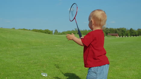 toddler holding badminton racket in green field. cute boy jumping in air