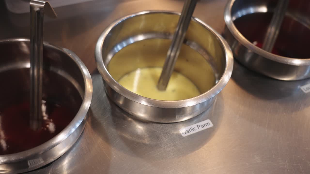 4K slow motion parallax footage of chicken wing sauces in dispensers including barbecue, garlic parmesan, and Louisiana hot sauce in a commercial kitchen setting