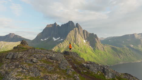 drone crane over hiker reveal majestic jagged senja mountain by fjord in sunset