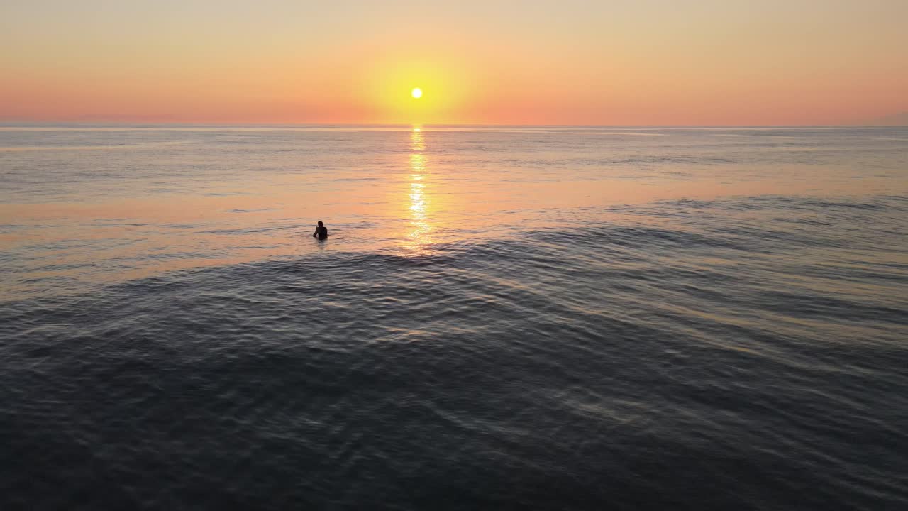 A single surfer at sunset waiting for a wave