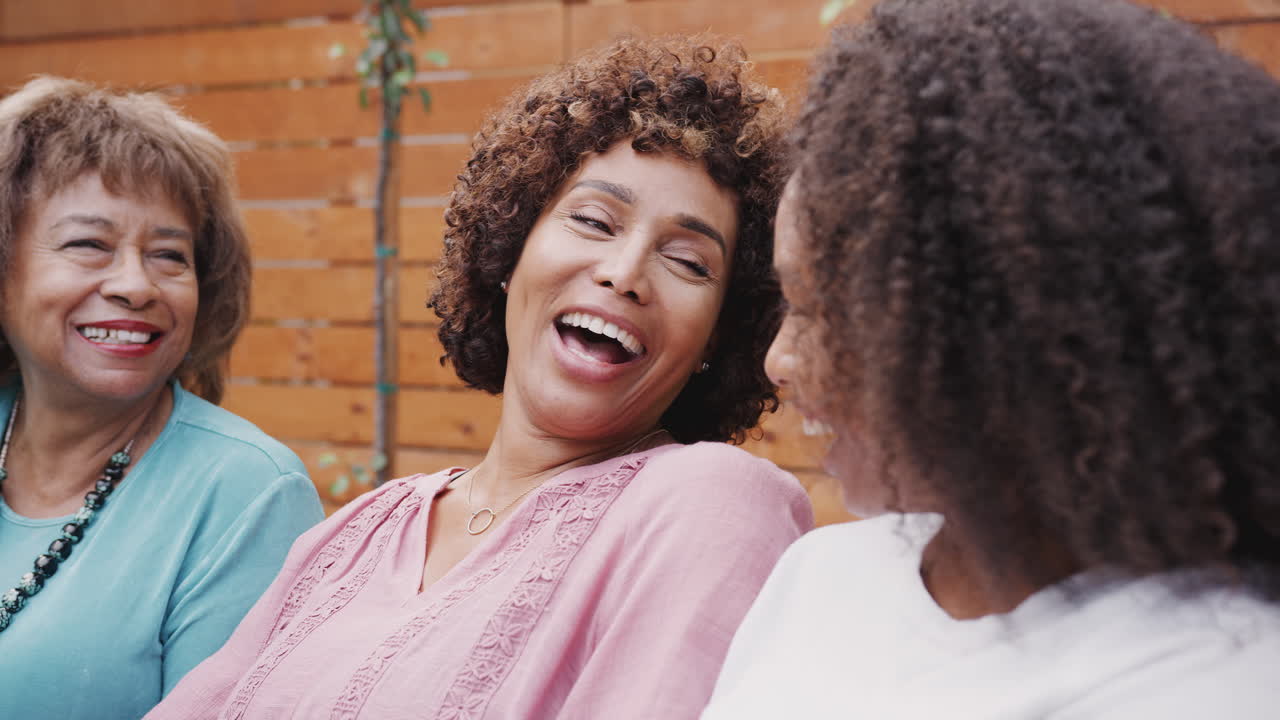 Three generations of female family members talking and laughing together outdoors, close up