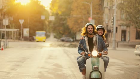 Glücklicher-Kerl-Mit-Langen-Lockigen-Haaren-In-Einem-Jeanshemd-Fährt-Mit-Seiner-Glücklichen-Freundin-In-Einem-Weißen-Helm-Auf-Einem-Motorrad-Mit-Eingeschalteten-Scheinwerfern-Bei-Sonnenaufgang-An-Einem-Sonnigen-Sommermorgen