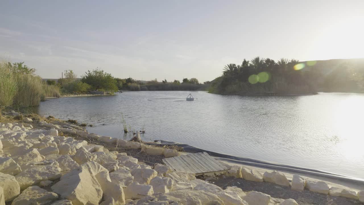 Water reservoir at Neot Smadar Kibbutz shows a paddle aerator operating on the lake, surrounded by arid desert and agriculture areas, illustrating water management systems, slow motion dolly in.