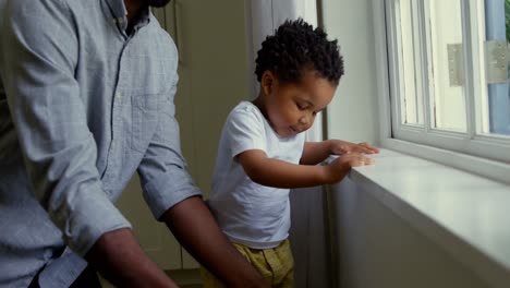 Sección-Media-De-Un-Joven-Padre-Negro-Jugando-Con-Su-Hijo-En-El-Alféizar-De-Una-Ventana-En-Una-Casa-Cómoda-4k