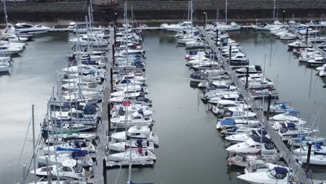 Scenic-luxurious-waterfront-harbour-apartment-village-yachts-and-sailboats-under-mountain-coastline-orbit-left-aerial-view