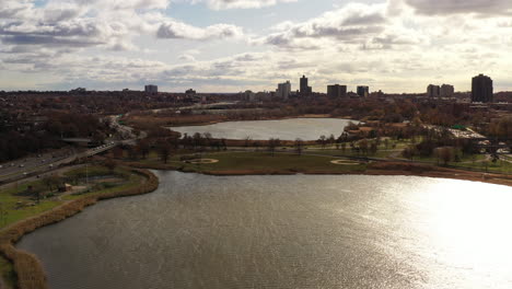 Plataforma-Rodante-Aérea-Sobre-Un-Lago-En-Un-Día-Nublado-Con-Campos-De-Béisbol-A-La-Vista