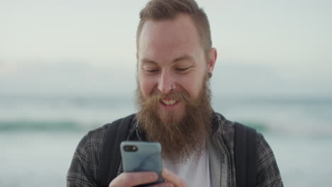 retrato de un joven hipster usando un teléfono inteligente sonriendo disfrutando de los mensajes de texto navegando en línea mensajería en la playa compartiendo experiencia de vacaciones