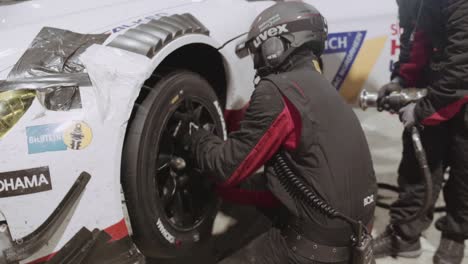 pit crew mechanic changing slick tire on a bmw race car at night in the pit lane during the adac nurburgring twentyfour hour race.