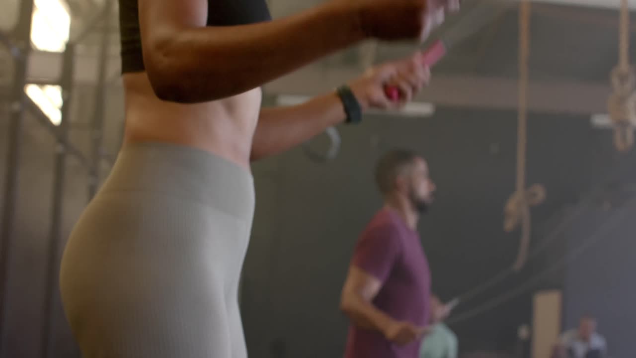 sección media de una mujer y un hombre diversos entrenando en un gimnasio saltando la cuerda, en cámara lenta