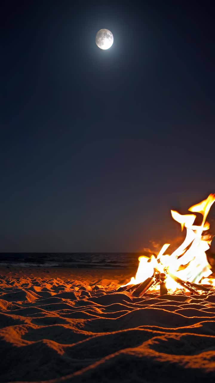 Uma filmagem de vídeo em ângulo baixo de uma fogueira na praia sob a lua cheia, capturando o céu noturno sereno
