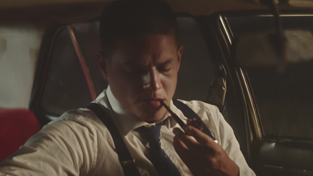 밤에 빈티지 자동차에서 파이프를 피우는 남자