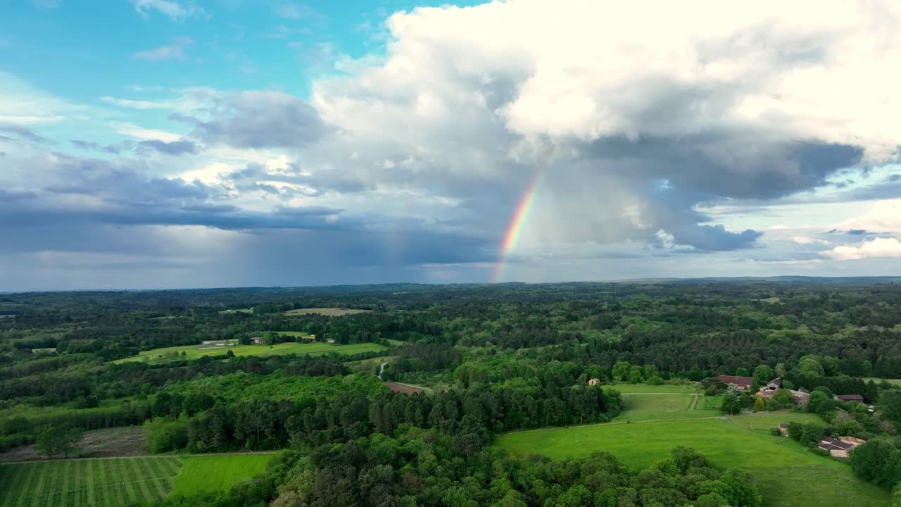Landsbygdsfält och skog upplysta av en klar regnbåge mot en molnig himmel. Drönarspårningsbild visar de livfulla färgerna i det franska landskapet efter regn.