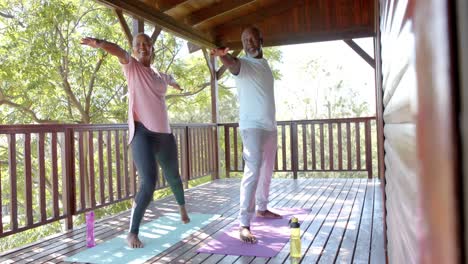 Happy-senior-african-american-couple-practicing-yoga-on-mats-on-sunny-terrace,-slow-motion