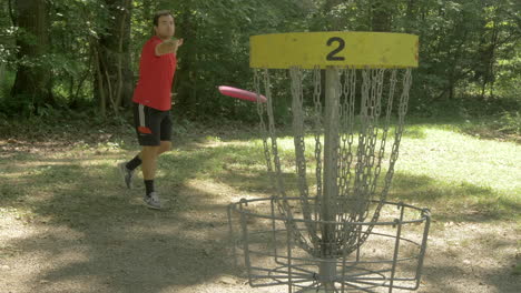 man scoort een basket in discgolf in het bos en viert heel enthousiast in slow motion feest