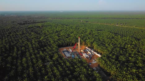 Cinematic-4K-Drone-Footage-of-Onshore-Drilling-Rig-equipment-structure-for-oil-exploration-and-exploitation-in-the-middle-of-jungle-surrounded-by-palm-oil-trees-during-sunset-and-high-oil-price